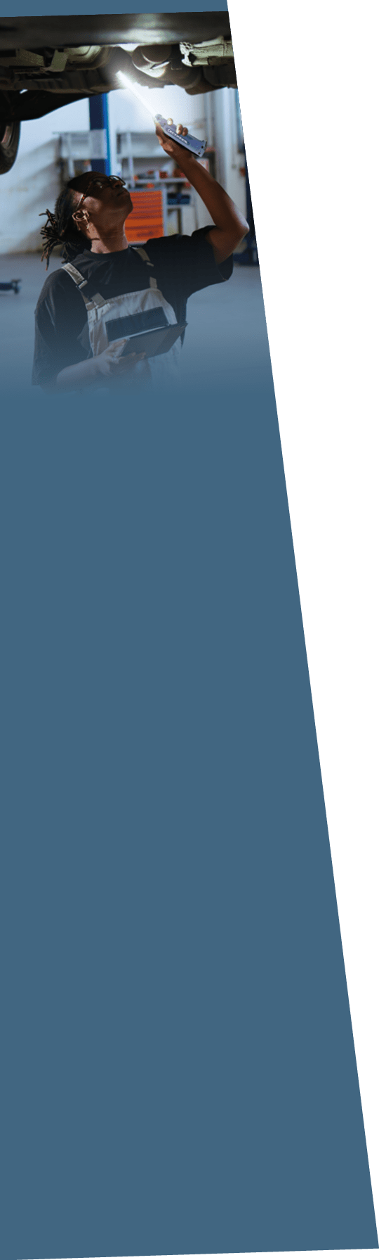 Qualified engineer underneath suspended car in repair shop, using work light to check for damages during maintenance. Expert using professional tool and tablet to examine vehicle on overhead lift